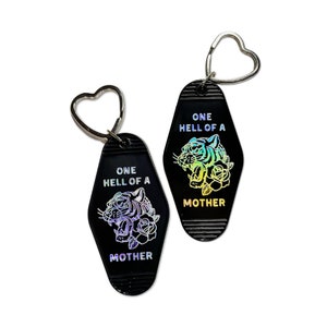 May include: Two black keychains with a tiger and roses design. The keychains are shaped like motel keys and have the text "One Hell of a Mother" on them.