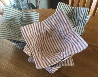 May include: A collection of handmade bowl cozies in various striped patterns. The cozies feature blue and white, red and white, and green and white stripes. These fabric bowl covers are designed to keep food warm.