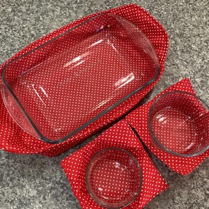 May include: A set of clear glass baking dishes, including a rectangular casserole dish and two round bowls, resting on red polka dot fabric. The dishes are arranged on a gray countertop, suggesting a kitchen setting.