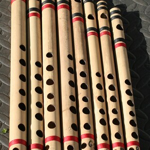 May include: A collection of bamboo flutes of varying lengths, arranged diagonally. Each flute has a natural wood tone with black and red bands. Some flutes are labeled with musical notes like D#, F#, F, G#, and B.