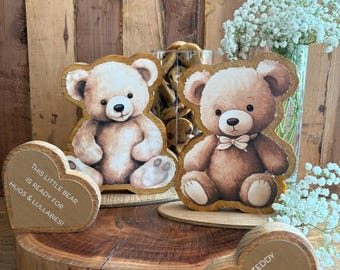 May include: Two wooden bear-shaped cutouts with printed teddy bear illustrations and two heart-shaped wooden plaques. One heart reads, "THIS LITTLE BEAR IS READY FOR HUGS & LULLABIES!" and the other reads, "FROM ONE TEDDY TO ANOTHER YOU'RE GOING TO BE BEARY LOVED!"