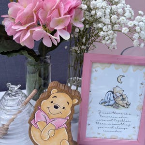 May include: A wooden cutout of Winnie the Pooh wearing a pink shirt, a glass honey jar with a wooden dipper, and a pink-framed print featuring Winnie the Pooh and Piglet with the text: If ever there is a tomorrow when we're not together, there is something you must always remember.