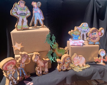 May include: Wooden figurines of Toy Story characters, including Woody, Buzz Lightyear, Jessie, Bo Peep, Rex, Mr. Potato Head, and Hamm. The figurines are painted in bright colors and are arranged on cardboard boxes.