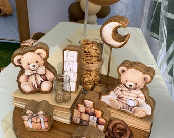 May include: Wooden centerpiece with a brown and white teddy bear, a crescent moon, and wooden blocks that spell "BABY". The centerpiece is on a wooden round base with a brown and white gift box, a wooden car, and a brown pretzel.
