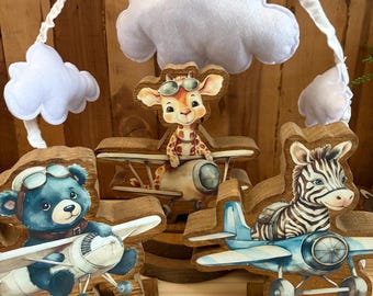 May include: A whimsical baby mobile featuring a blue bear, giraffe, and zebra in wooden airplanes. The mobile includes white felt clouds and a wooden arch. The animals wear aviator goggles. The planes are painted in blue and beige.