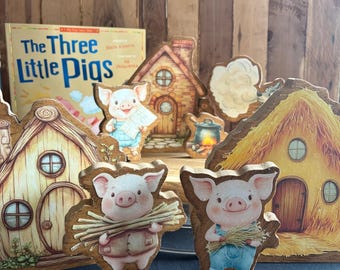 May include: Wooden figurines depicting scenes from "The Three Little Pigs" story. The set includes houses, pigs, and a book with the title. The figurines are painted with bright colors and have a rustic, handcrafted appearance. The book is visible in the background.