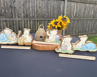 May include: Wooden Winnie the Pooh figurines with various characters, including Tigger and Piglet. The figurines are on a wooden base with quotes. A decorative beehive and sunflowers are also present.