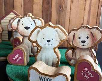 May include: Wooden dog figurine set with three dogs, a bone, and two hearts that say "Puppy Love". The dogs are painted in shades of brown and white and have cute faces. The set is on a green felt base.