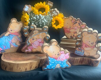 May include: A set of wooden Winnie the Pooh character figurines. The figurines are painted in bright colors and feature Winnie the Pooh, Piglet, Tigger, and Eeyore. The figurines are arranged on a wooden slice with a sunflower bouquet in the background.