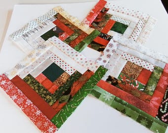 May include: A patchwork quilt block with a log cabin pattern in red, green, white, and brown fabrics. The block is made up of squares and rectangles of different sizes and colors.