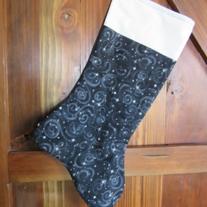 May include: A black and white Christmas stocking with a white cuff and a swirling pattern of stars and white lines on a black background.