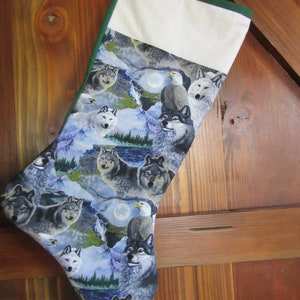 May include: A green and white Christmas stocking with a winter scene featuring wolves and an eagle. The stocking has a white cuff with a green trim.