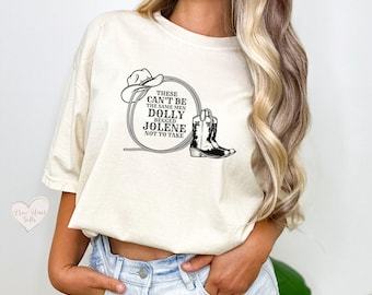 May include: Cream-colored t-shirt featuring a circular graphic with a cowboy hat, a cowboy boot, and the text "These Can't Be The Same Men Dolly Begged Jolene Not To Take". The shirt has short sleeves and a relaxed fit.