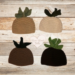 May include: Four crochet hats in the shape of succulents are displayed on a wooden surface. The hats are in shades of brown, tan, and black, each with green leaf accents. The hats are handmade and have a textured appearance.