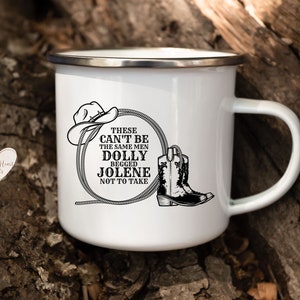 Könnte beinhalten: Weißer Emaillebecher mit silbernem Rand und Henkel. Der Becher zeigt eine schwarze Grafik eines Cowboyhuts, eines Seils und eines Stiefels mit dem Text "THESE CAN'T BE THE SAME MEN DOLLY BEGGED JOLENE NOT TO TAKE."