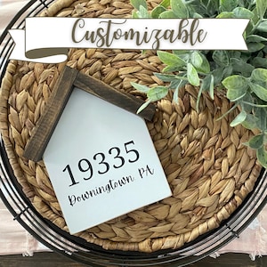 May include: A white wooden house-shaped sign with black text that reads "1935 Downingtown, PA". The sign is sitting on a woven wicker surface.