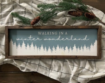 May include: A wooden sign with a blue background and white text that reads "Walking in a winter wonderland". The sign features a silhouette of a snowy forest.