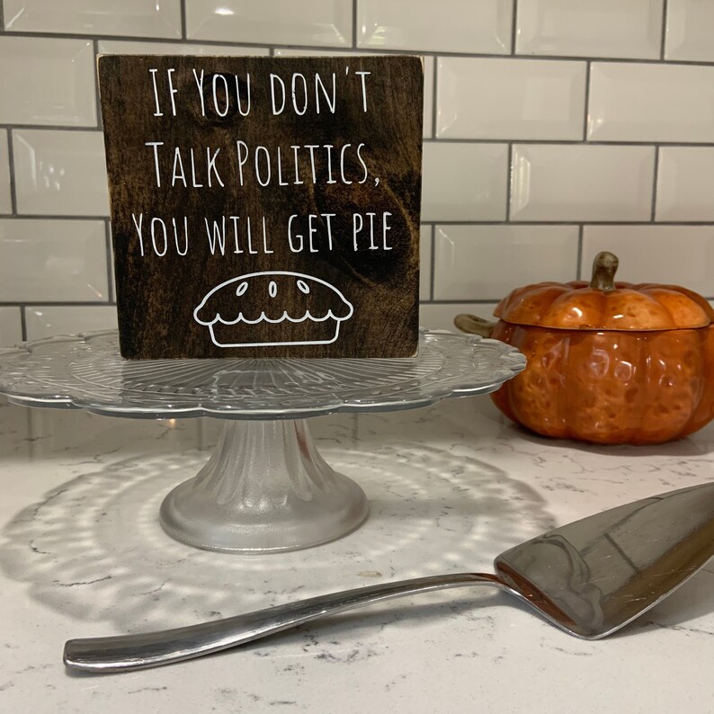 Peut inclure: Une pancarte en bois avec le texte "Si vous ne parlez pas de politique, vous aurez de la tarte." La pancarte est d&eacute;cor&eacute;e d'un contour blanc d'une tarte.