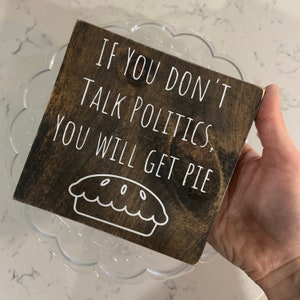 Peut inclure: Une pancarte en bois avec le texte "Si vous ne parlez pas de politique, vous aurez de la tarte" et un contour blanc d'une tarte.