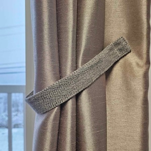 May include: A pair of brown satin curtains with a gray and white herringbone patterned tieback.