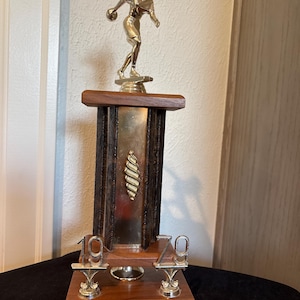 May include: A trophy featuring a silver-toned figure of a person throwing a discus, mounted on a wooden base with dark textured pillars. The trophy includes silver-toned numbers 19 and 79, and a plaque reading WINTER WONDERS 1ST PLACE TEAM 1979.