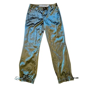 May include: Olive green satin pants with a subtle sheen. The pants have two front pockets, a button and zipper closure, and drawstrings at the ankles. The brand name "Mudd" is visible on the waistband.