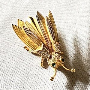 May include: A gold-toned brooch in the shape of a dragonfly with clear and green rhinestones.