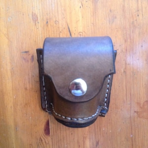 May include: A small brown leather pouch with a white stitching detail and a silver button closure.