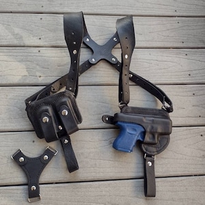 May include: A black leather shoulder holster with a blue handgun and a separate black leather strap with two pockets.
