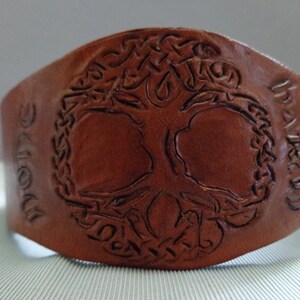 May include: Brown leather bracelet with a tree of life design and the words "Believe" and "Hope" embossed on the sides.