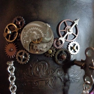 May include: A steampunk-style top hat with a variety of gears and clockwork elements attached to the top. The hat is made of brown leather and has a silver chain hanging from it.