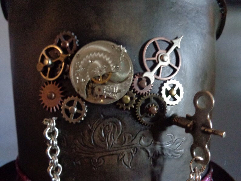 May include: A steampunk-style top hat with a variety of gears and clockwork elements attached to the top. The hat is made of brown leather and has a silver chain hanging from it.