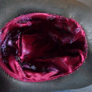 May include: The inside of a black hat with a burgundy satin lining. The lining has a floral pattern in a lighter shade of purple.