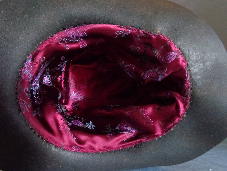 May include: The inside of a black hat with a burgundy satin lining. The lining has a floral pattern in a lighter shade of purple.