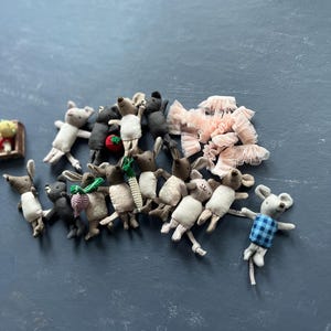 Peut inclure: Une collection de poupées souris miniatures faites à la main, de différentes couleurs et poses. Certaines souris tiennent des carottes miniatures, des fraises et d'autres petits objets. Une souris porte une chemise à carreaux bleue. Un groupe de nœuds en dentelle rose est également présent.