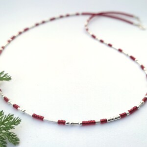 Op de afbeelding: Een delicate ketting gemaakt met afwisselende zilveren en rode kralen. De ketting is geregen op een dun rood koord.