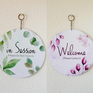 Könnte beinhalten: Zwei runde Holzschilder mit Blumendesigns und Text. Das Schild links sagt "in Session Please Do Not Disturb" und das Schild rechts sagt "Welcome Please Come in".