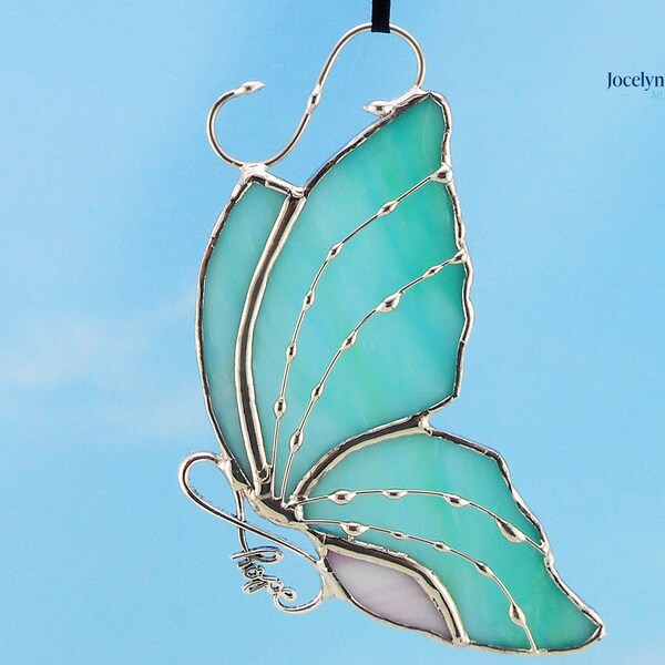 Vidriera de mariposa aqua y rosa.  Su cuerpo representa un signo del infinito, un regalo que se debe dar para enfatizar el amor, como un consuelo de duelo.