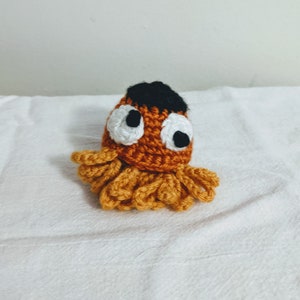 May include: A crocheted octopus toy with orange and brown body, black hair, white eyes, and yellow tentacles.