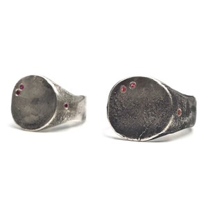 May include: Two silver signet rings with a textured finish. Each ring has three small red gemstones set into the top of the ring.
