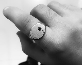 May include: A silver signet ring with an oval shaped top featuring a palm tree design.