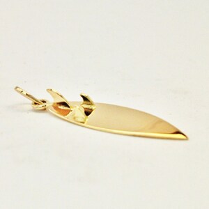 May include: A gold-colored surfboard charm with three fins. The charm is designed to be worn as a necklace or bracelet.