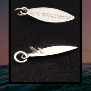May include: Silver charm in the shape of a surfboard with the text "You Can not Stop The Waves But You Can Learn How To Surf!" engraved on it.