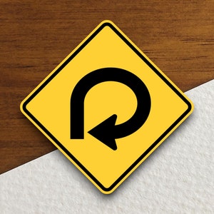 May include: A yellow, diamond-shaped road sign featuring a black U-turn arrow. The sign has a black border and is set against a wood grain background.