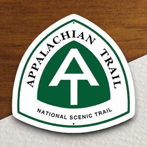 May include: White metal sign with a green triangle and white letter A inside. The sign reads "Appalachian Trail National Scenic Trail".