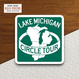Puede incluir: Una pegatina cuadrada con fondo verde oscuro que presenta un contorno blanco de la región del lago Michigan. El texto "LAKE MICHIGAN" aparece en la parte superior y una banda blanca en el centro contiene el texto "CIRCLE TOUR" en blanco.