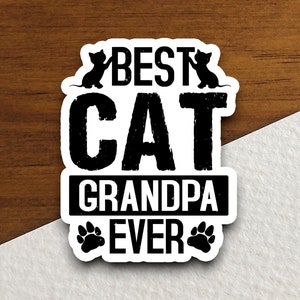 Pu&ograve; includere: Adesivo bianco e nero con il testo "Best Cat Grandpa Ever" in un font usurato. Due silhouette di gatti neri sono sopra il testo e due impronte di zampe nere sono sotto il testo.