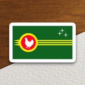 May include: A rectangular sticker with a green background and a white border. The design features a white chicken inside a red circle with a yellow border. Two yellow horizontal lines and three white stars are also present.