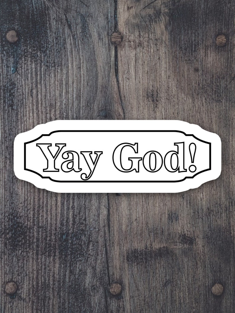 May include: White sticker with black outline and the text "Yay God!" on a dark brown wooden background.