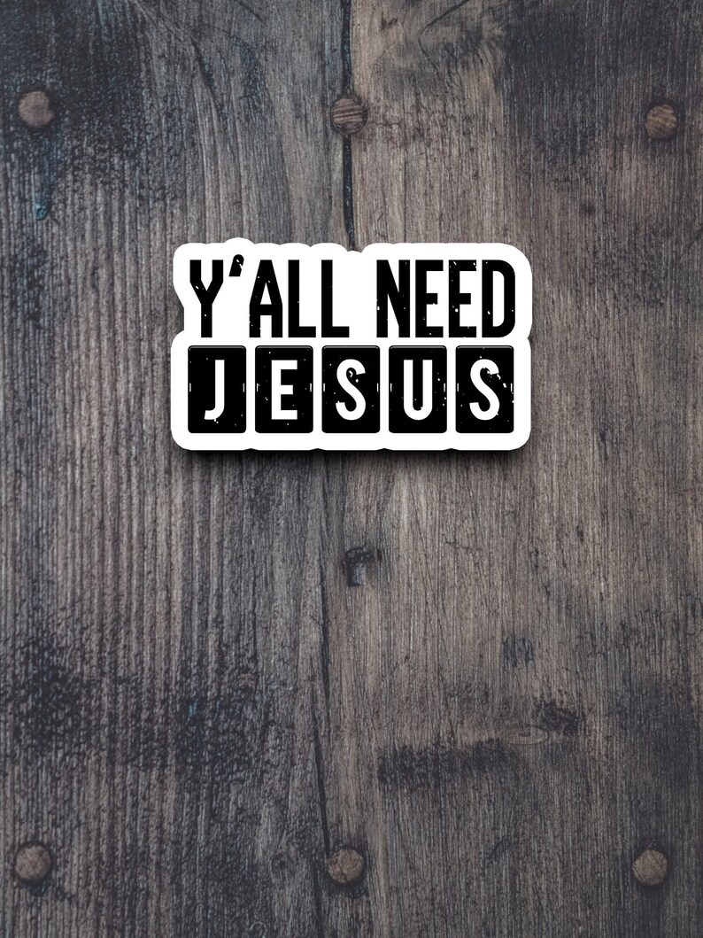 Peut inclure: Un autocollant blanc avec du texte noir sur un fond en bois. L'autocollant dit "Y'all need Jesus" avec le mot "Jesus" dans des carr&eacute;s individuels.